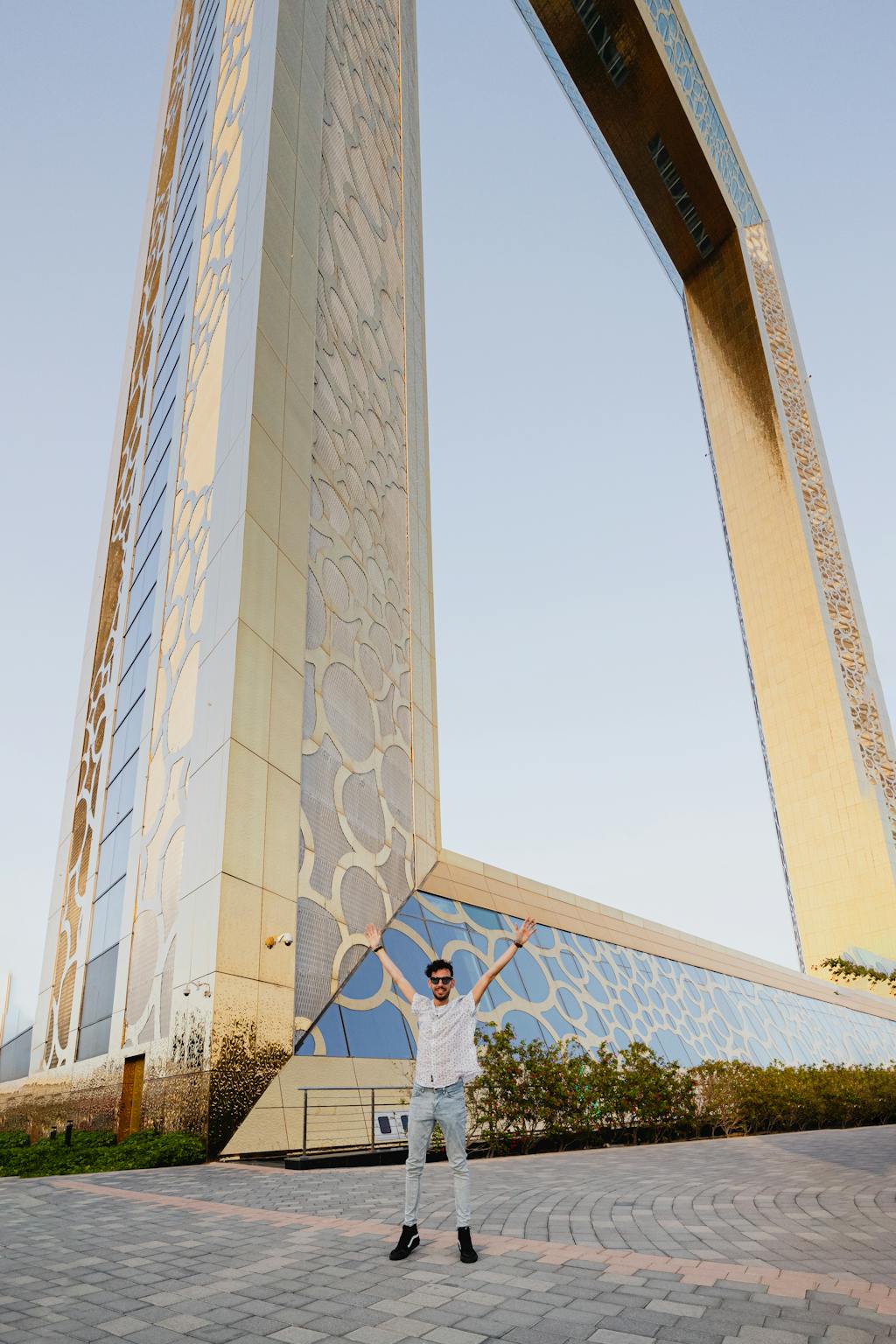 A man poses with arms raised in front of the iconic Dubai Frame during sunset, UAE.