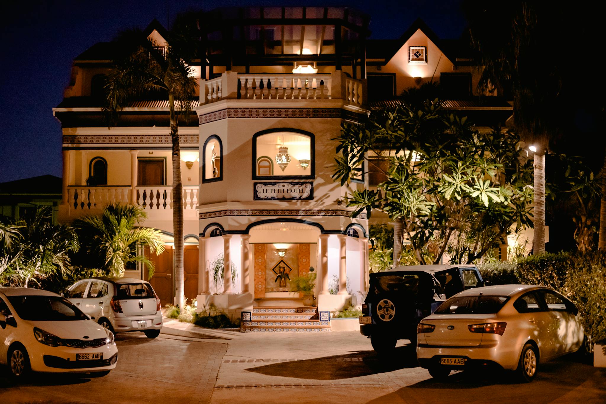 Illuminated villa facade with parked cars at night, showcasing architecture and luxury.